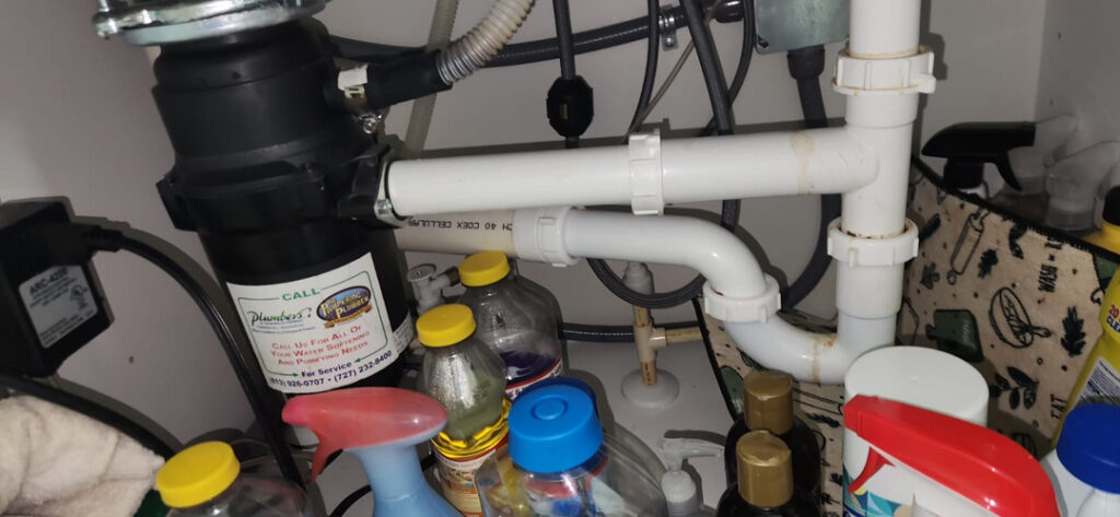 a garbage disposal unit and plumbing beneath a sink surrounded by various cleaning supplies and a towel