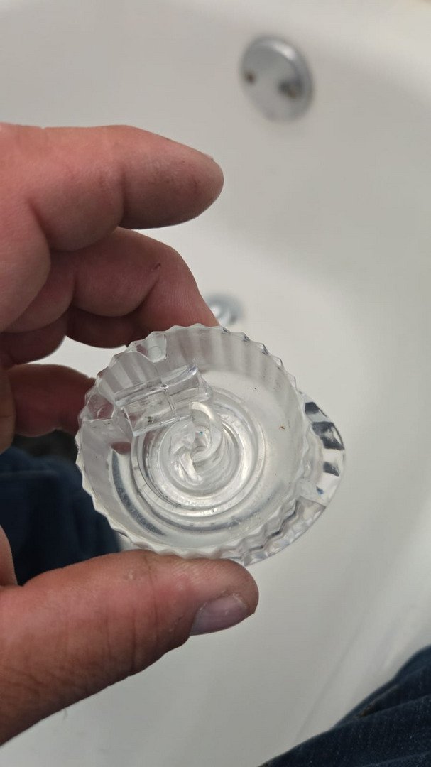 a hand holding a clear round bathtub drain cover above a white bathtub surface