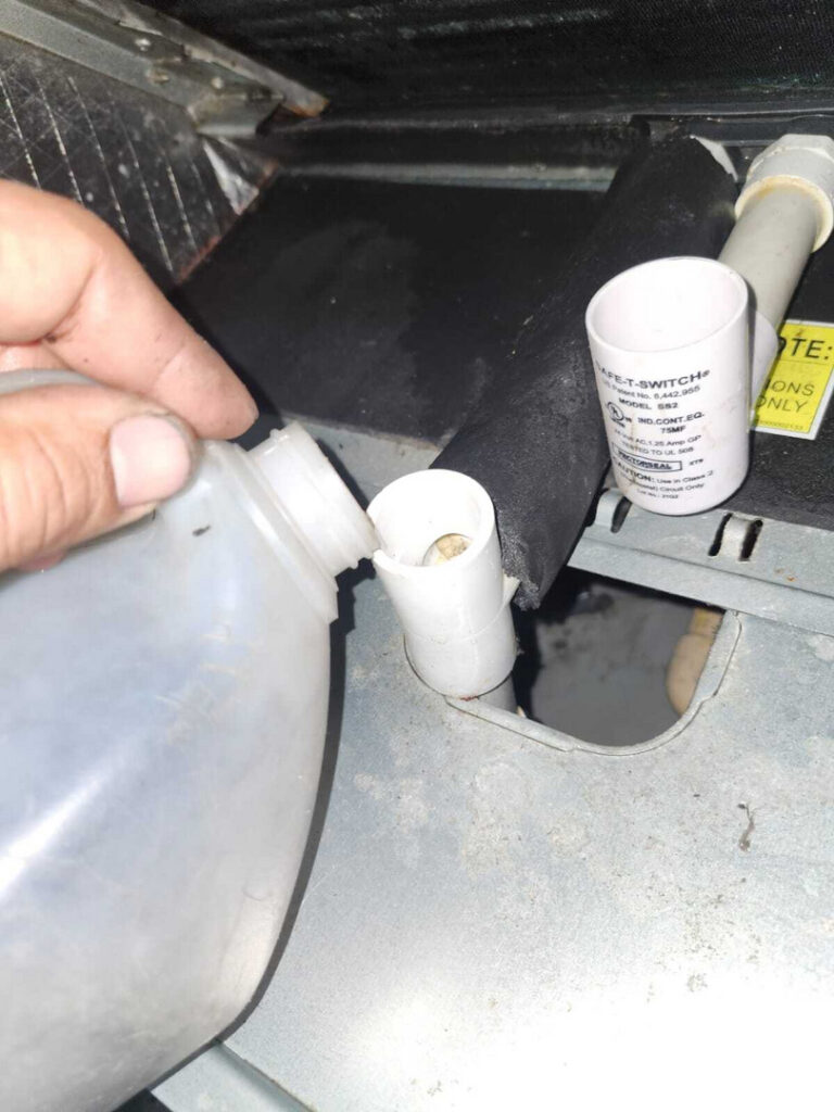 a hand pouring liquid into a pvc pipe likely for maintenance of an hvac system or drain line