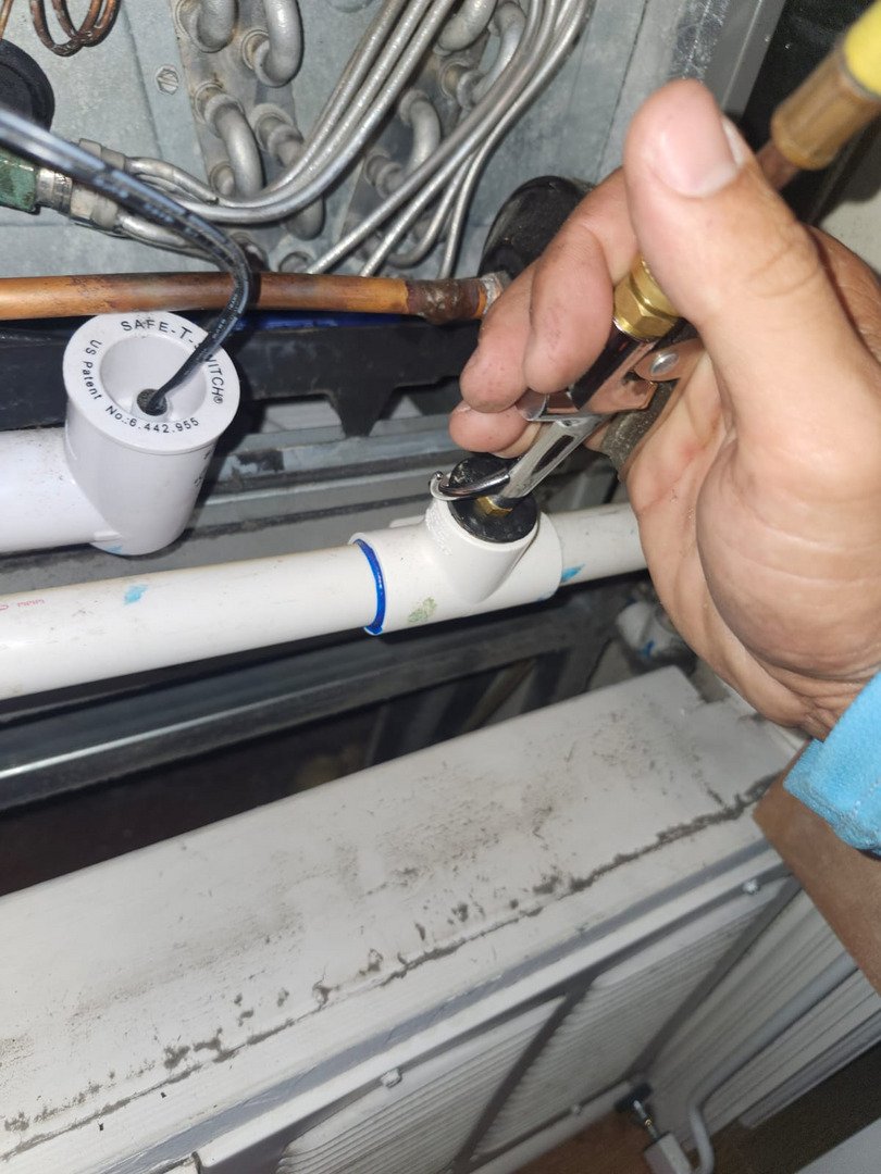 a person tightening a valve on a plumbing system using an adjustable wrench near copper and plastic pipes