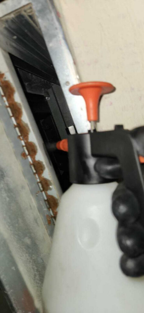 a person using a spray bottle near a vent likely performing maintenance or cleaning in a heating and cooling system