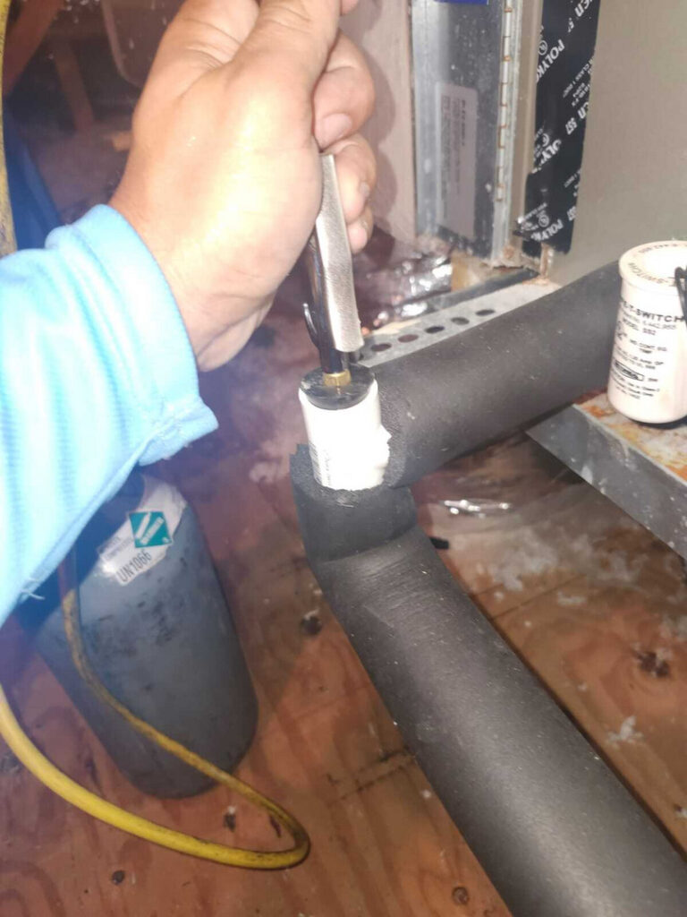 a technician tightening a fitting on a pipe likely related to heating or cooling system maintenance