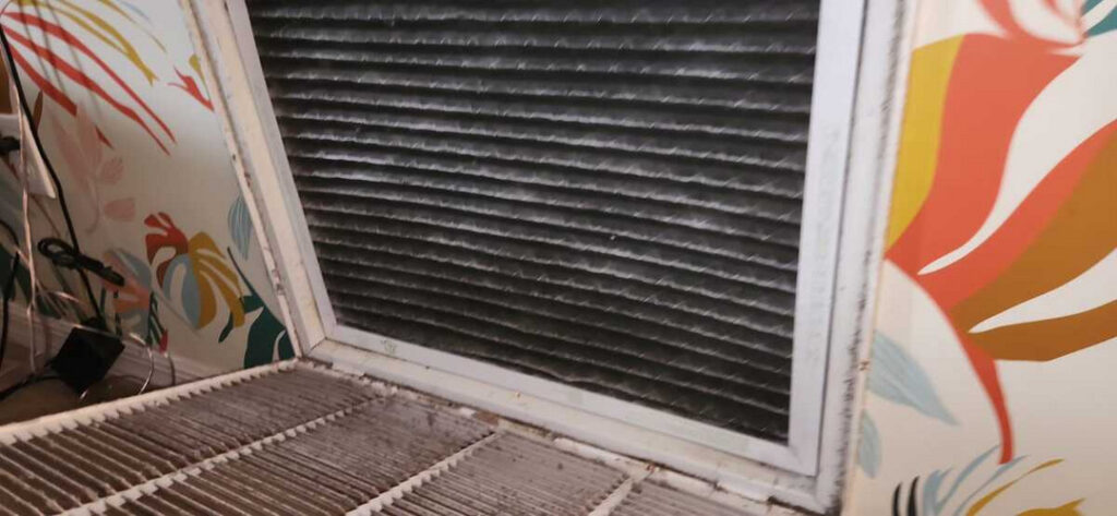 air filter removal showing heavy dirt buildup with a patterned wall in the background and visible electrical cords