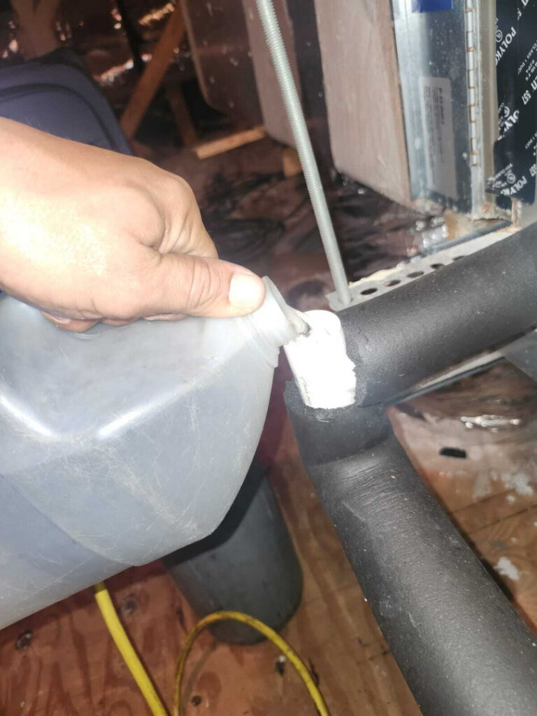 applying sealant or adhesive to a pipe joint in an attic or basement environment with visible insulation and tools nearby