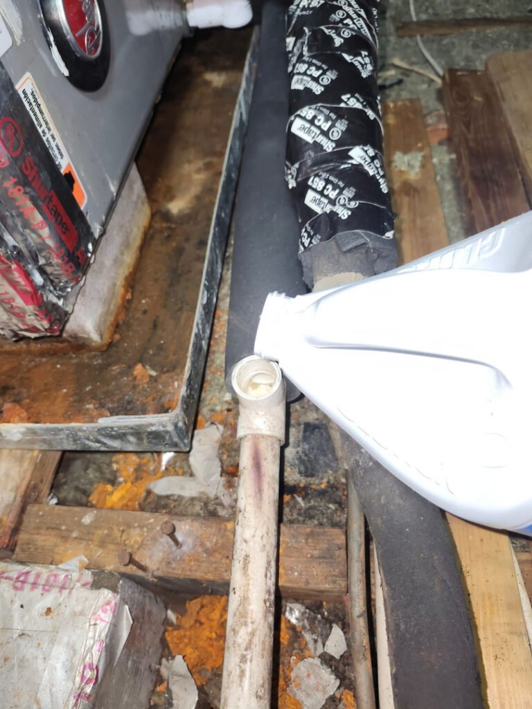 From one of our recent jobs: applying sealant to a plumbing joint with pipes and insulation visible in a cluttered space.