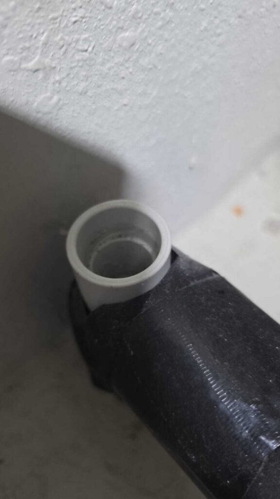 black and white pipe connection close up showing a white drain pipe fitting against a textured wall surface