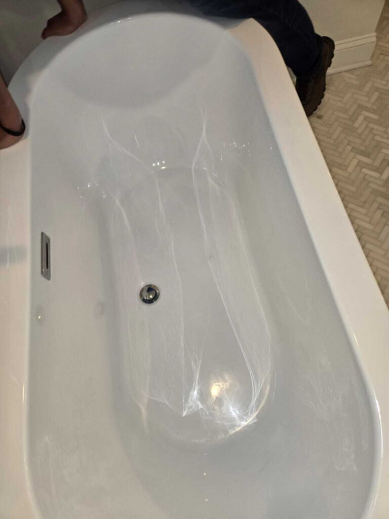 cleaning a white bathtub with visible reflections and light scratches present in the porcelain surface