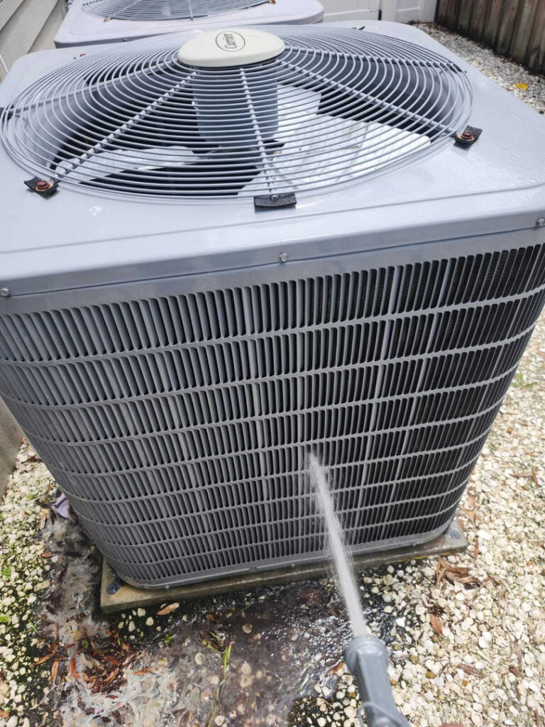 cleaning an outdoor air conditioning unit with a water spray removing dirt and debris from the exterior coils