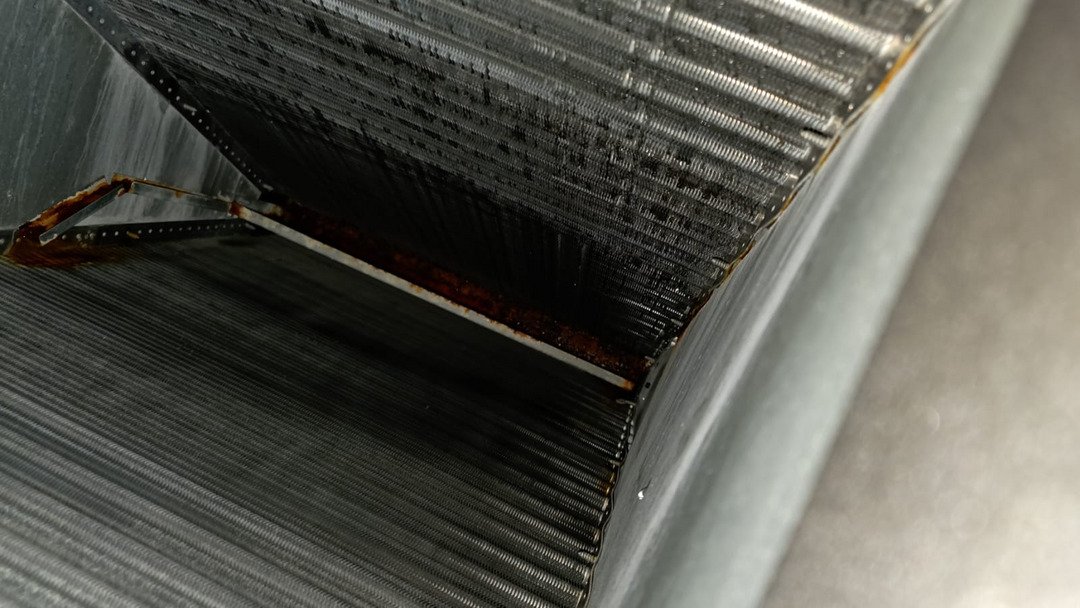 cleaning and inspecting a dirty air conditioning coil with visible rust and debris on the surface