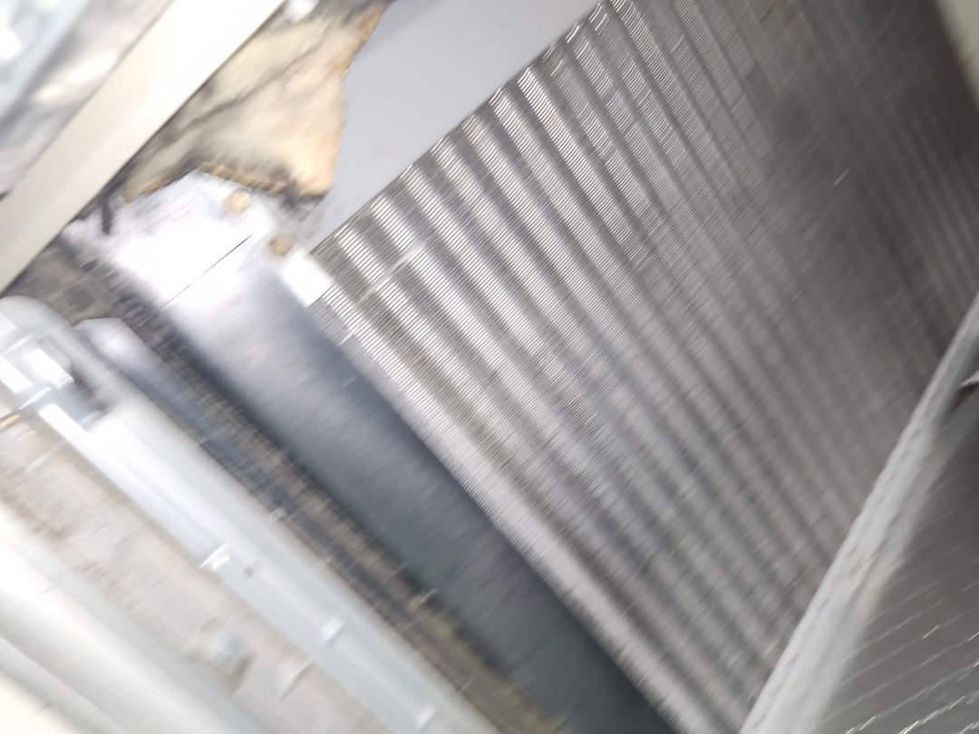 Cleaning Or Inspecting An Air Conditioning Unit With Visible Metal Fins And Components Likely Part Of Maintenance Service