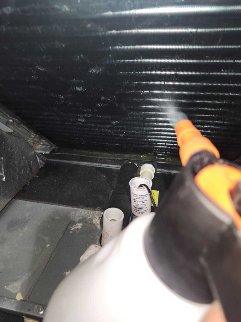 cleaning refrigerant coils using a spray nozzle and visible piping components and surfaces in a mechanical setting