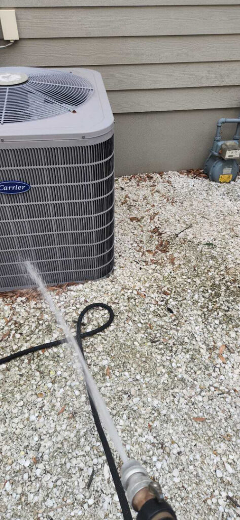 cleaning the exterior of an air conditioning unit using a pressure washer with water spraying from the nozzle