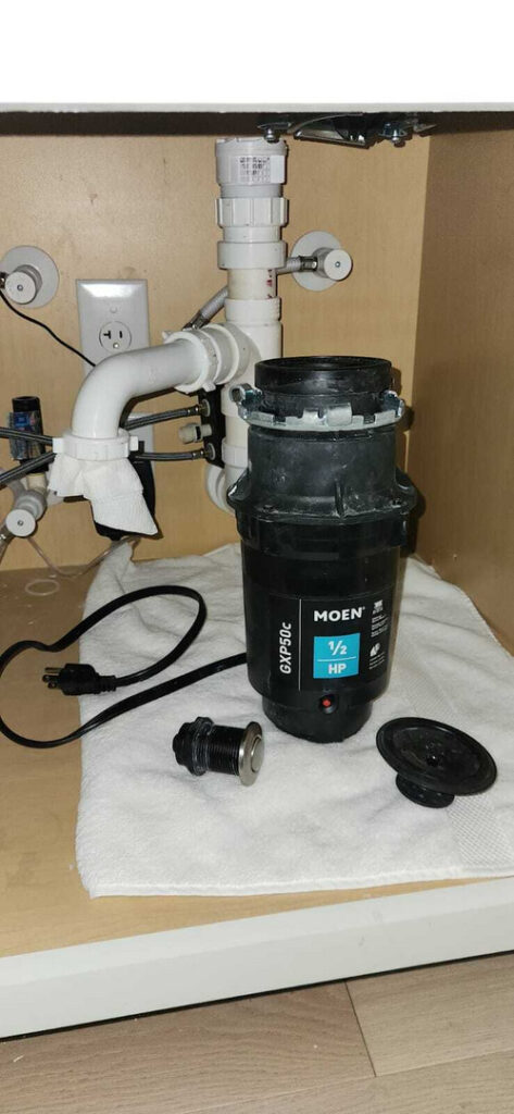 disassembled garbage disposal unit on a white towel with plumbing connections and components laid out beneath a kitchen sink