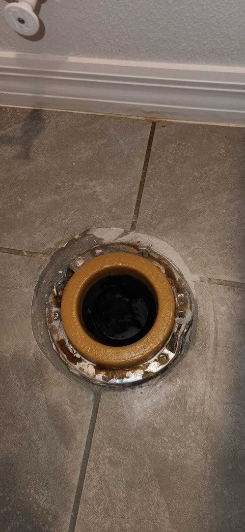 drain installation being performed on a tile floor with a visible wax ring and metal flange around the drain opening