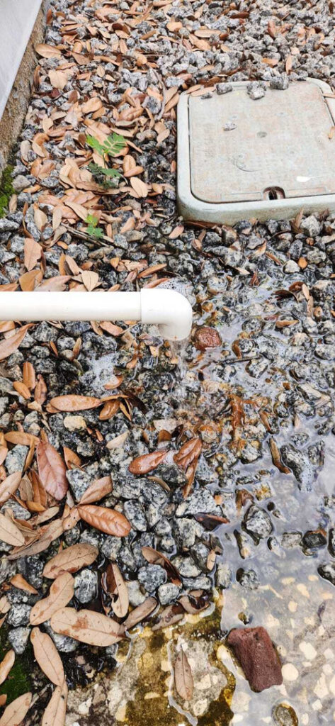 drain pipe discharging water onto gravel strewn with fallen leaves possibly indicating drainage or plumbing work being completed