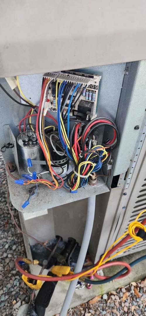 electrical panel of an outdoor cooling unit with various wires and connections visible and some mechanical components exposed