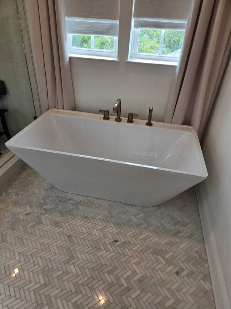 freestanding bathtub installation in a bathroom with marble herringbone tile and natural light from windows
