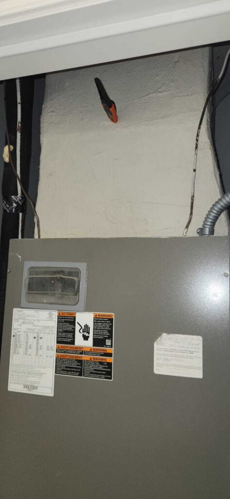 gray electrical panel mounted on wall with warning labels and wires visible on the side and top section of the panel