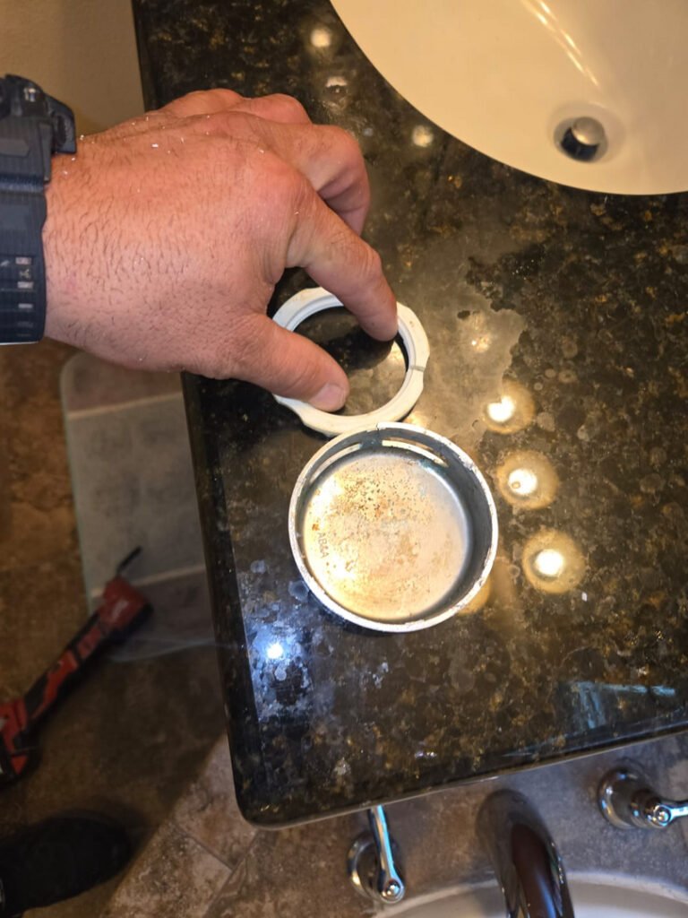 From one of our recent jobs: hand removing a drain cover from a bathroom sink for plumbing maintenance and inspection on a dark countertop.