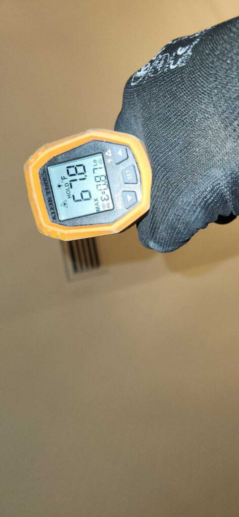 holding a thermal gun displaying temperature readings in a room likely related to heating or cooling assessment