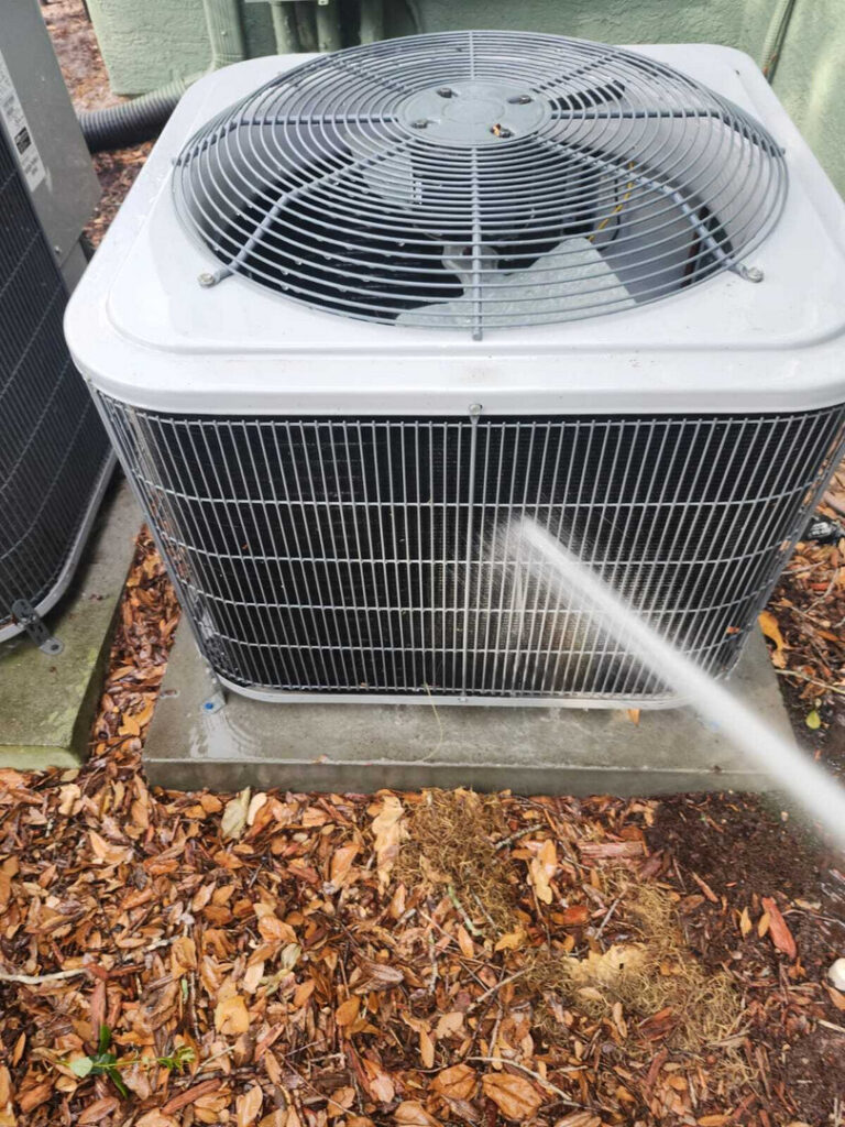 home therapist cooling heating and plumbing cleaning an air conditioning unit using a pressure washer with water on leaves