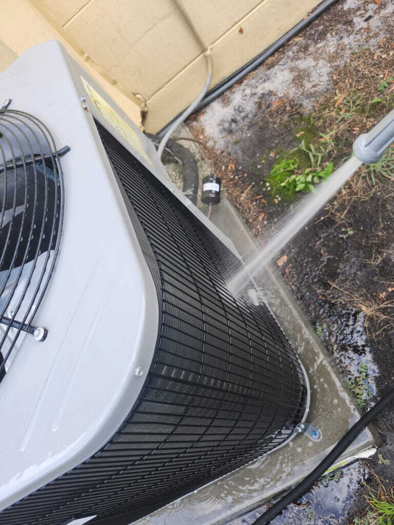 home therapist cooling heating and plumbing cleaning an outdoor air conditioning unit using a pressure washer to remove dirt and debris