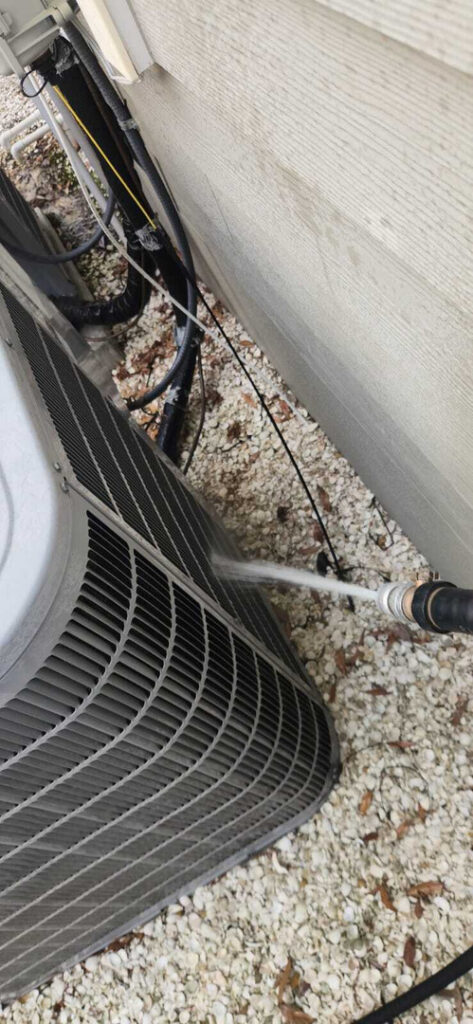 home therapist cooling heating and plumbing cleaning the condenser unit using a pressurized water hose on the exterior unit