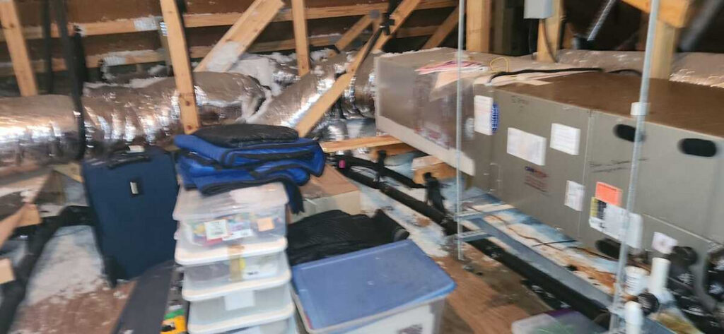 home therapist cooling heating and plumbing inspecting ductwork and equipment in an attic space with boxes and storage items present