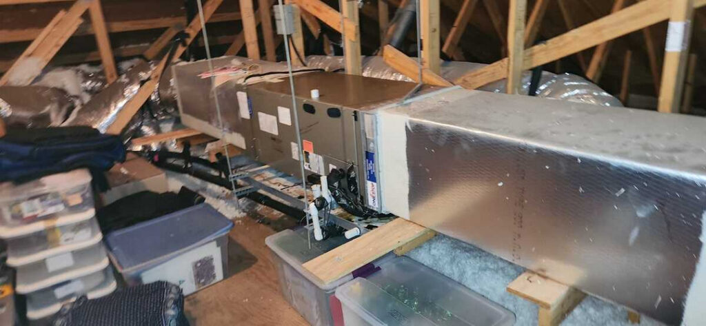 home therapist cooling heating and plumbing installing or servicing an air conditioning unit in an attic space with storage boxes nearby