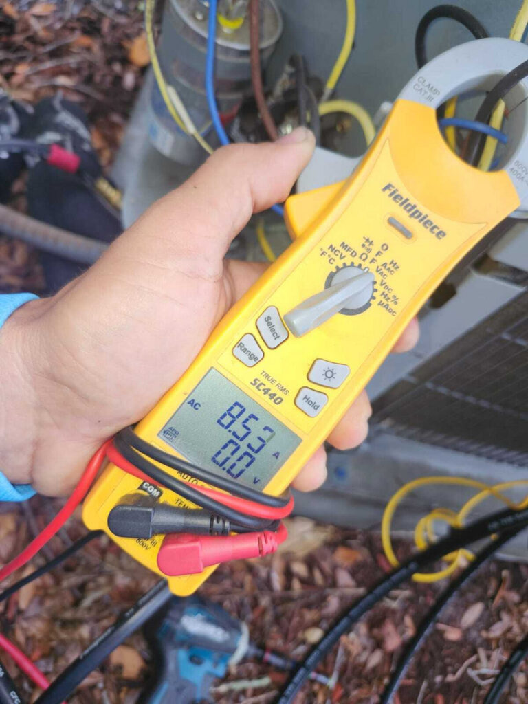 home therapist cooling heating and plumbing measuring electrical current with a clamp meter near hvac equipment