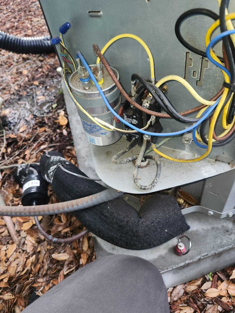 home therapist cooling heating and plumbing performing maintenance on electrical components of an outdoor unit with various wires and connections