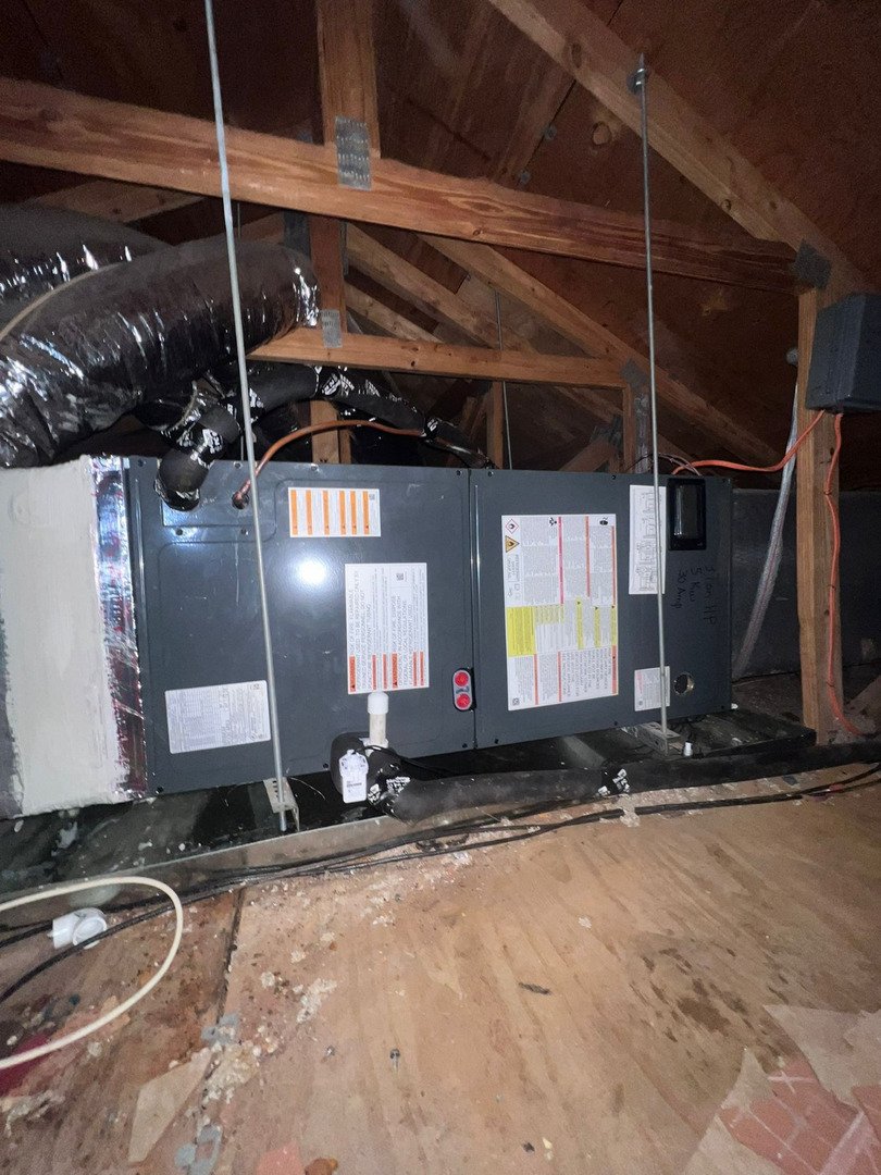 home therapist cooling heating and plumbing servicing an air conditioning unit in an attic space with exposed ductwork and wiring