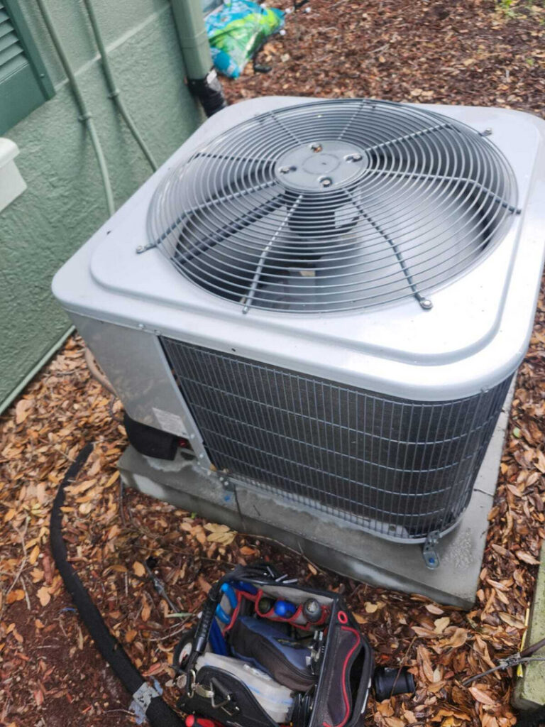 home therapist cooling heating and plumbing servicing an outdoor air conditioning unit with tools nearby on the ground