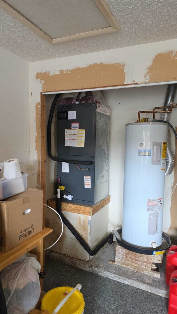 home therapist cooling heating and plumbing working on a gray furnace and a water heater in a utility room