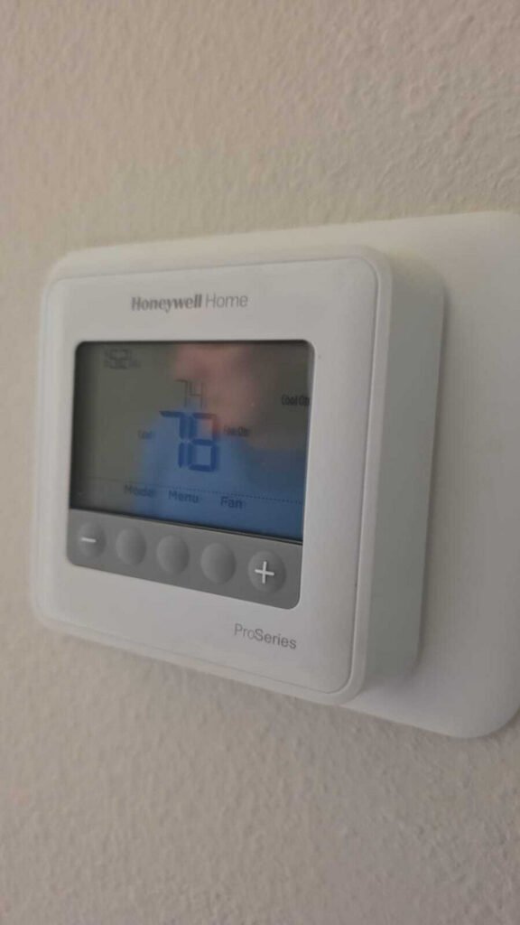 honeywell thermostat displaying indoor temperature and settings with a blue screen mounted on a wall