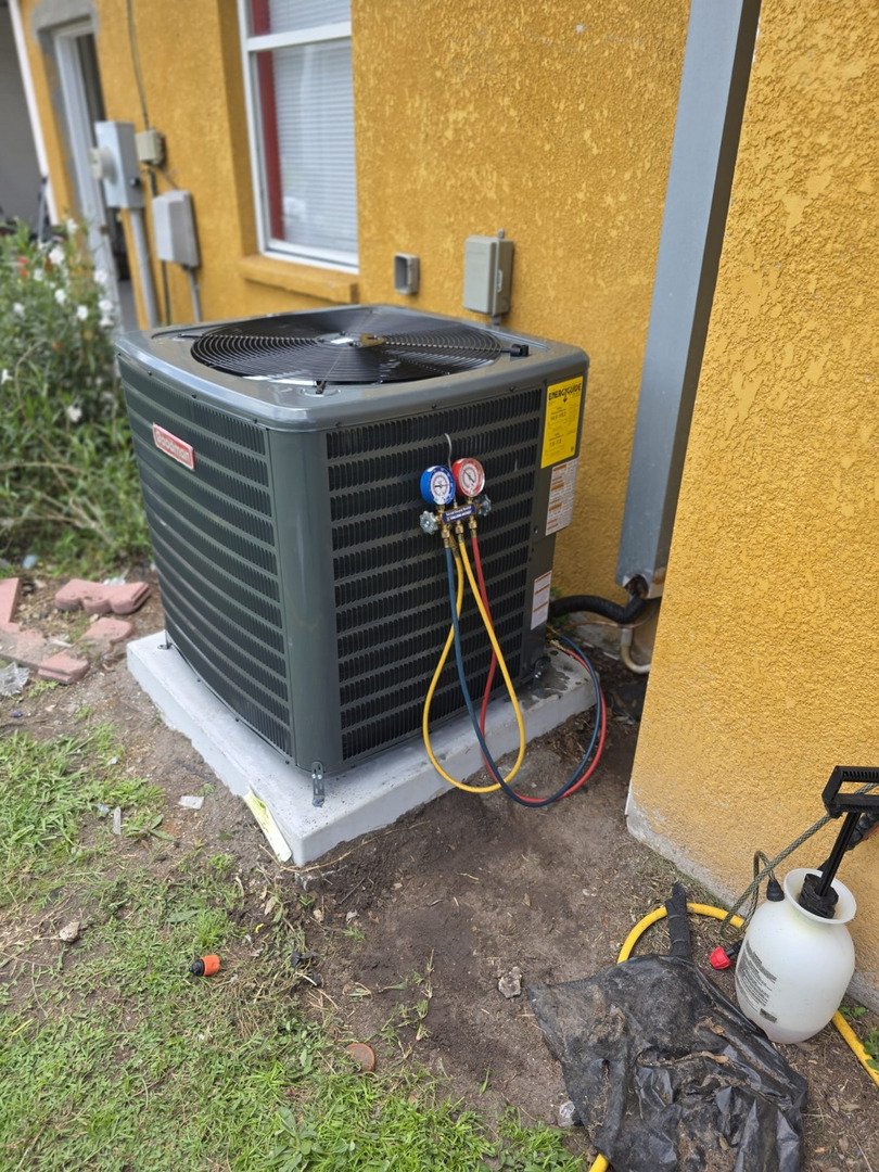 hvac technician servicing an air conditioning unit with gauges and hoses attached on a concrete pad near a wall