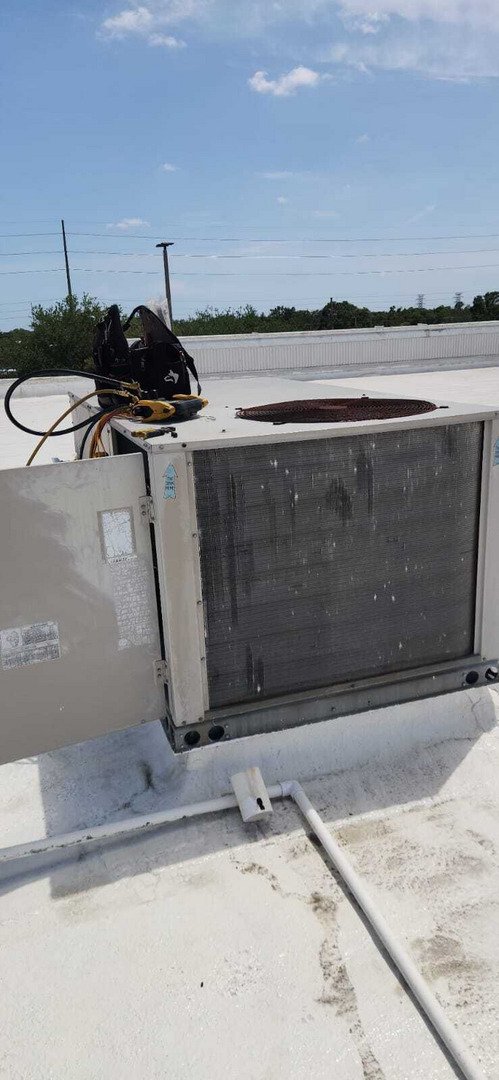 hvac unit being serviced on a rooftop with tools and equipment visible in the background and clear sky above