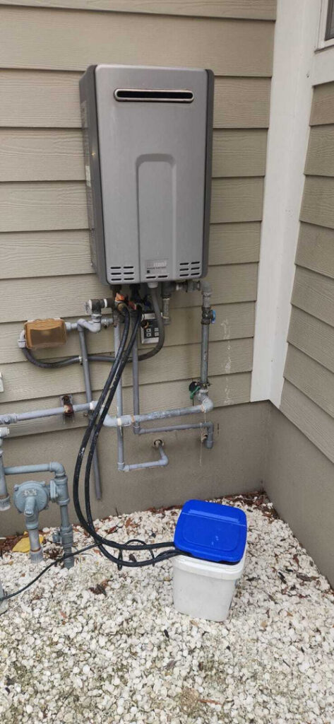 installation of a grey tankless water heater with connected plumbing and gas lines near a light gravel surface