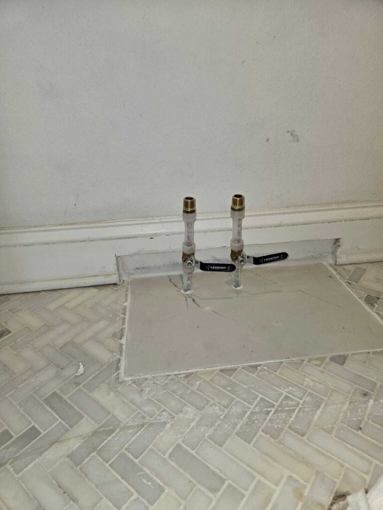 installation of plumbing valves in a tiled floor with visible grout lines and wall baseboard in the background
