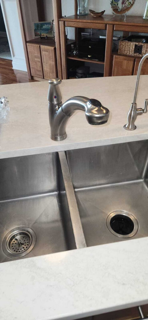 installing a new faucet in a stainless steel sink with a clean countertop and additional sprayer attachment