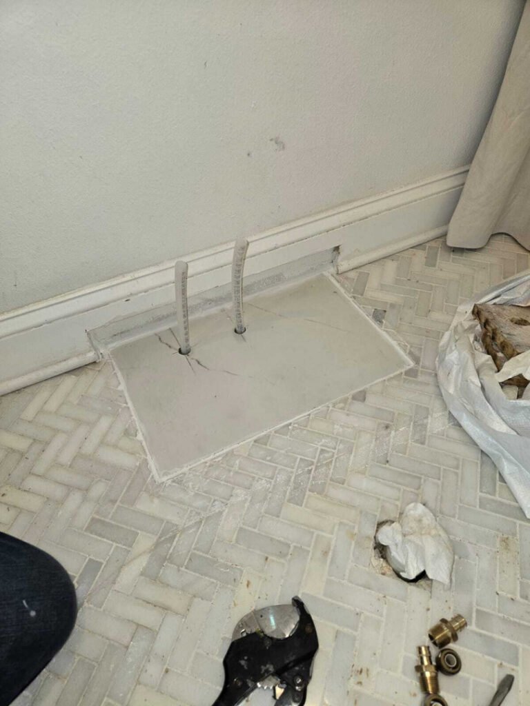 installing plumbing components near a wall with pipes visible on the floor and tools laid out nearby