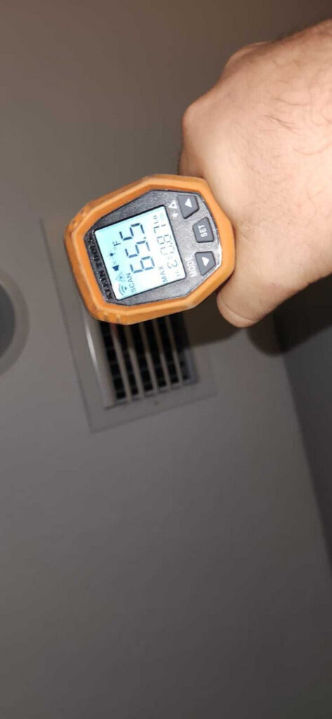 measuring air temperature with a handheld thermometer near a ceiling air vent showing a reading of sixty five point five degrees