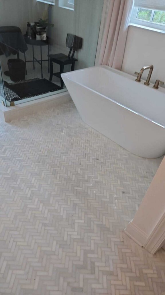 modern bathroom featuring a white freestanding tub with a herringbone patterned floor and glass shower enclosure