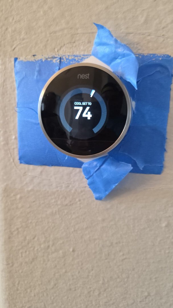 nest thermostat displaying a temperature setting of seventy four degrees on a wall with blue painter's tape around it
