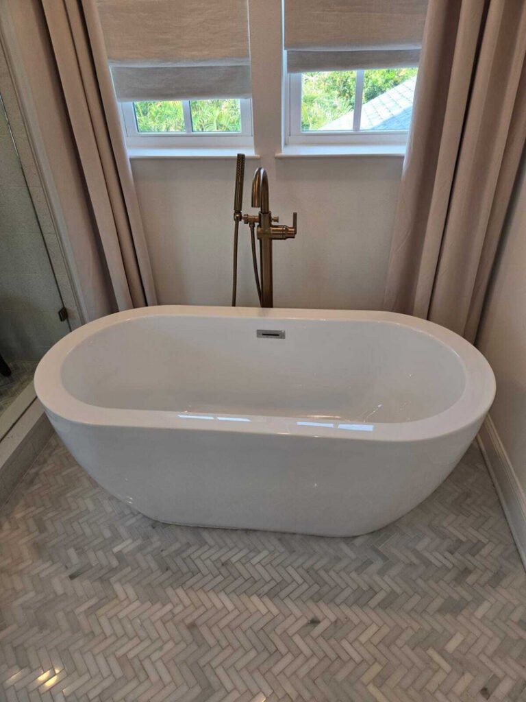 newly installed freestanding bathtub with modern faucet and herringbone tile floor in bright bathroom setting