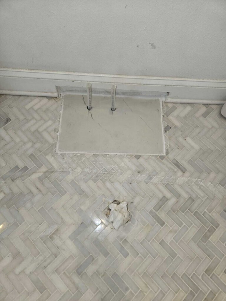 pipes installed in a tile floor area with a patch in the tile and visible cracks in the surrounding surface