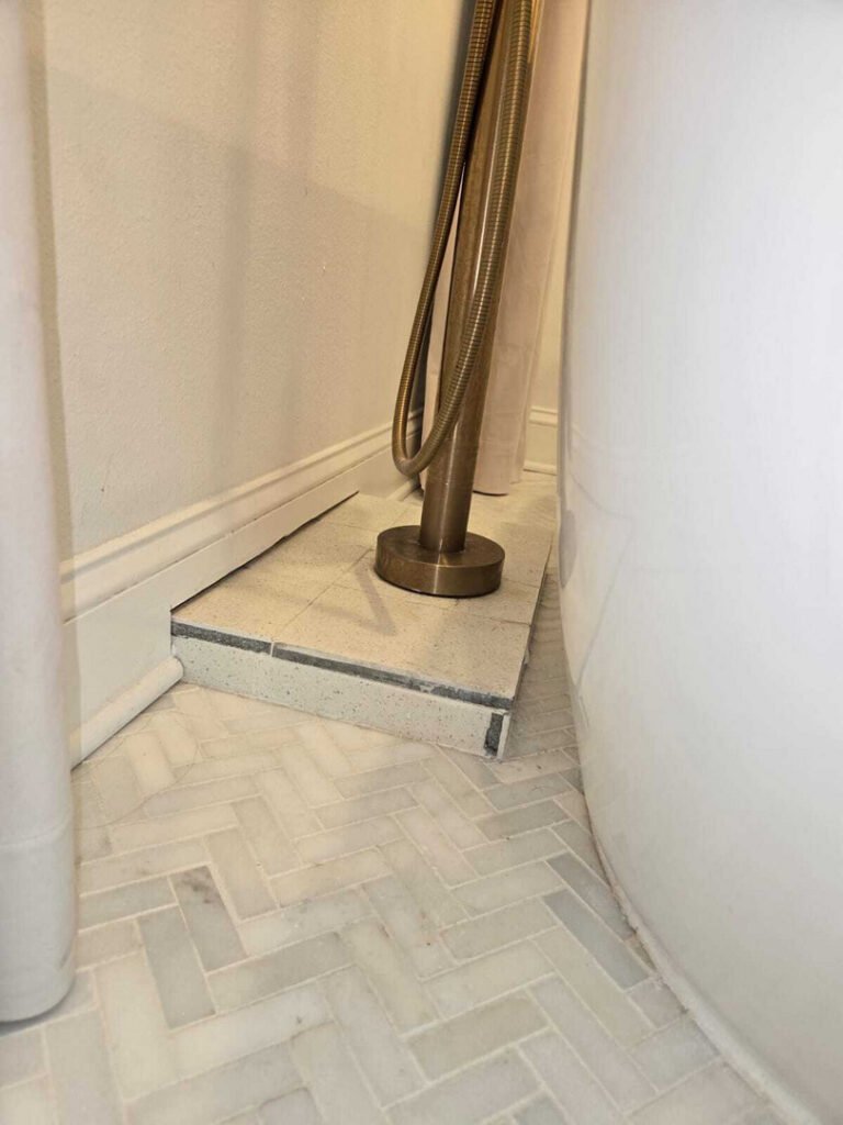 plumbing installation in a bathroom near a tub with a faucet and tiled floor visible
