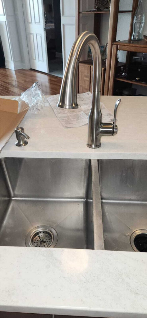 plumbing installation of a stainless steel faucet in a modern kitchen sink with double basins and a light countertop