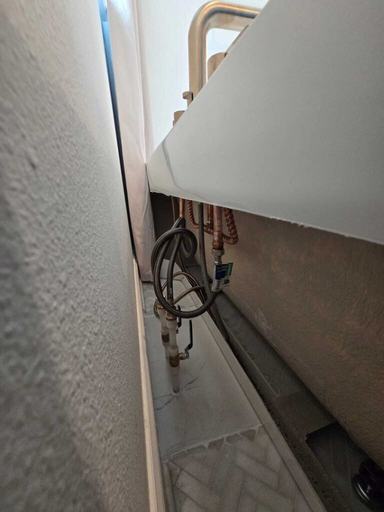 plumbing installation seen with pipes and connections near a bathtub in a tight space