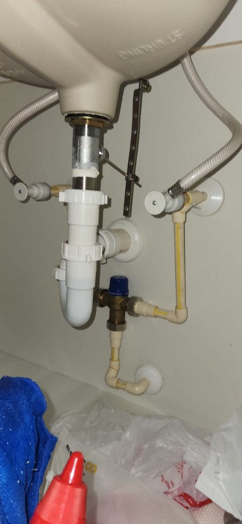 plumbing installation under a sink featuring pipes fittings and sealants with tools and materials nearby